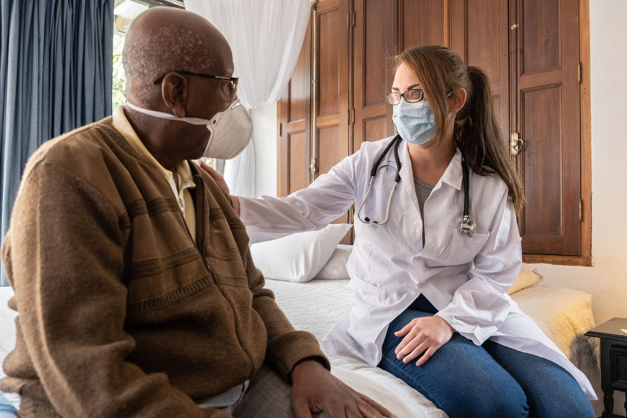 Doctor consoling senior patient at home - wearing face mask